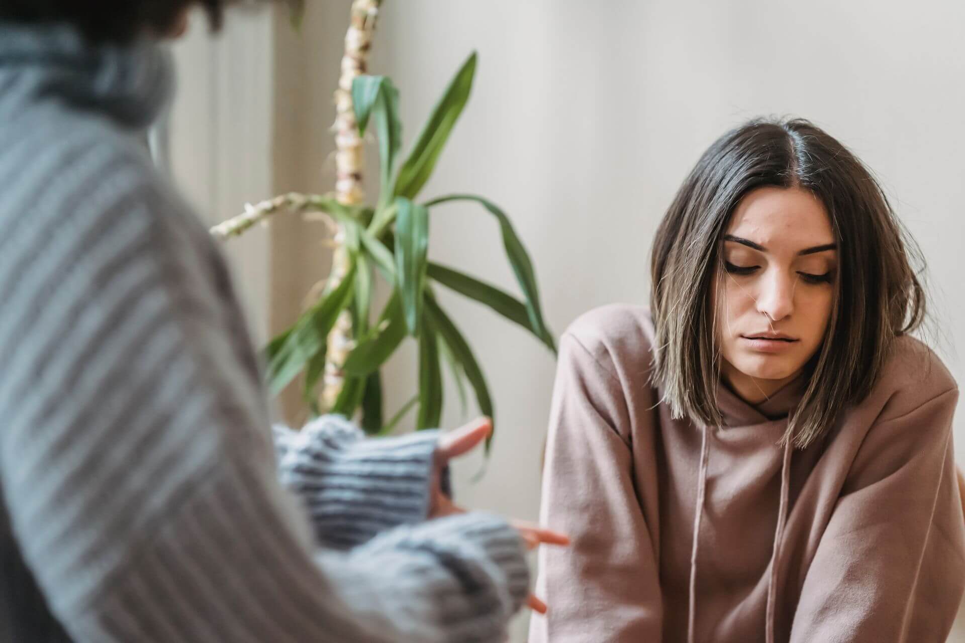 A grieving woman sitting quietly with her eyes lowered while someone nearby offers support