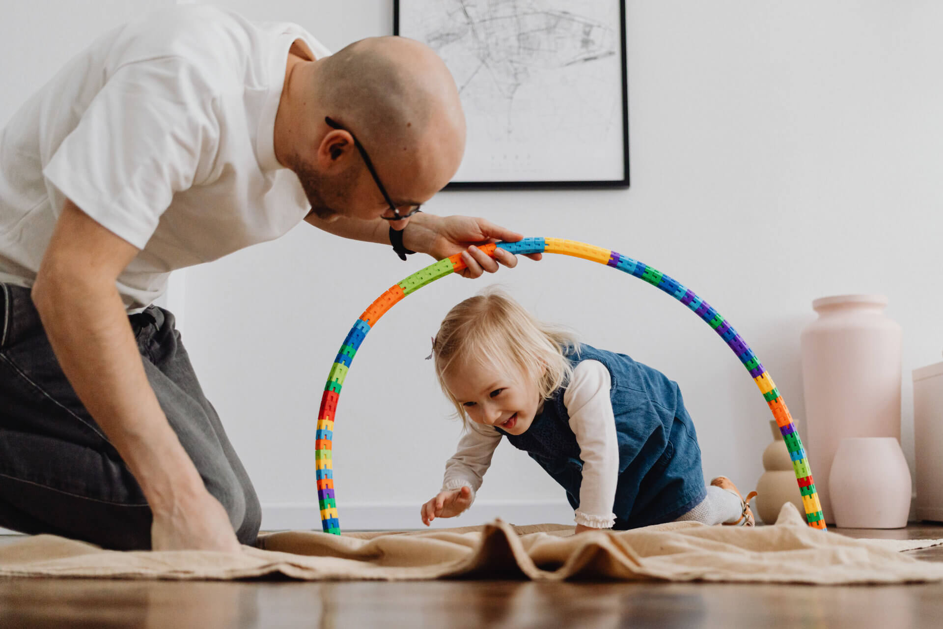 A caregiver and toddler sitting on the floor together, hands touching as they play with wooden blocks